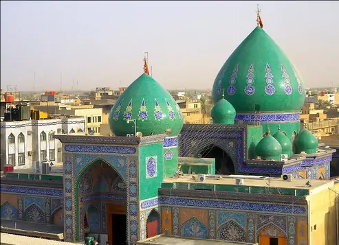 Two green tiled domes above a blue-and-green tiled facade with a pointed archway