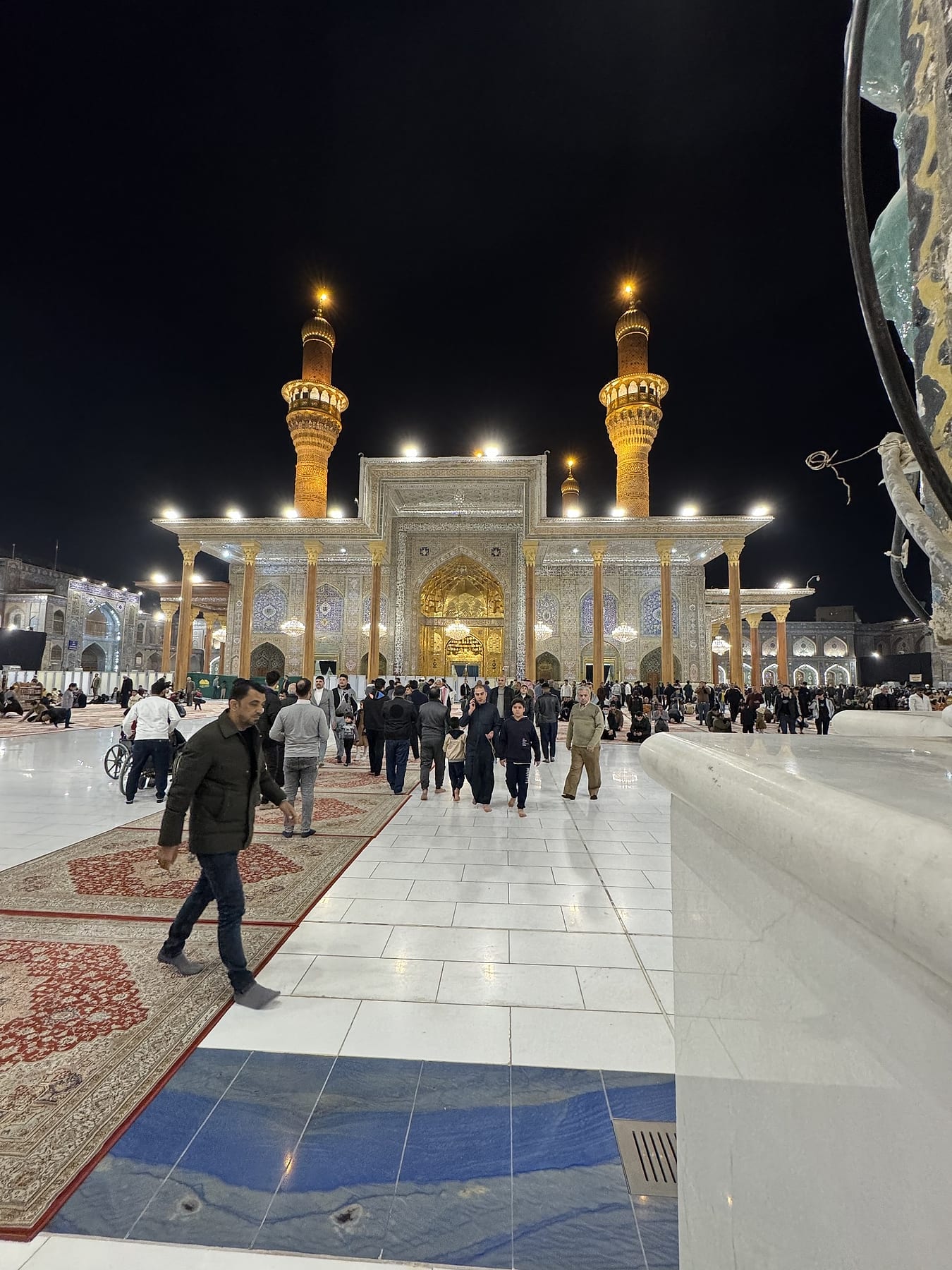 Visitors crossing the lit marble courtyard at night towards the gilded façade