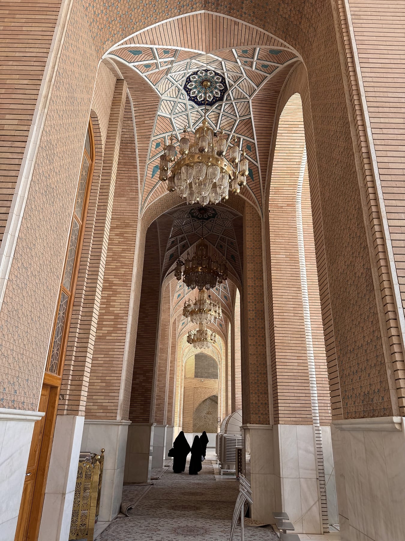 A tall brick corridor hung with chandeliers, with two visitors in the distance