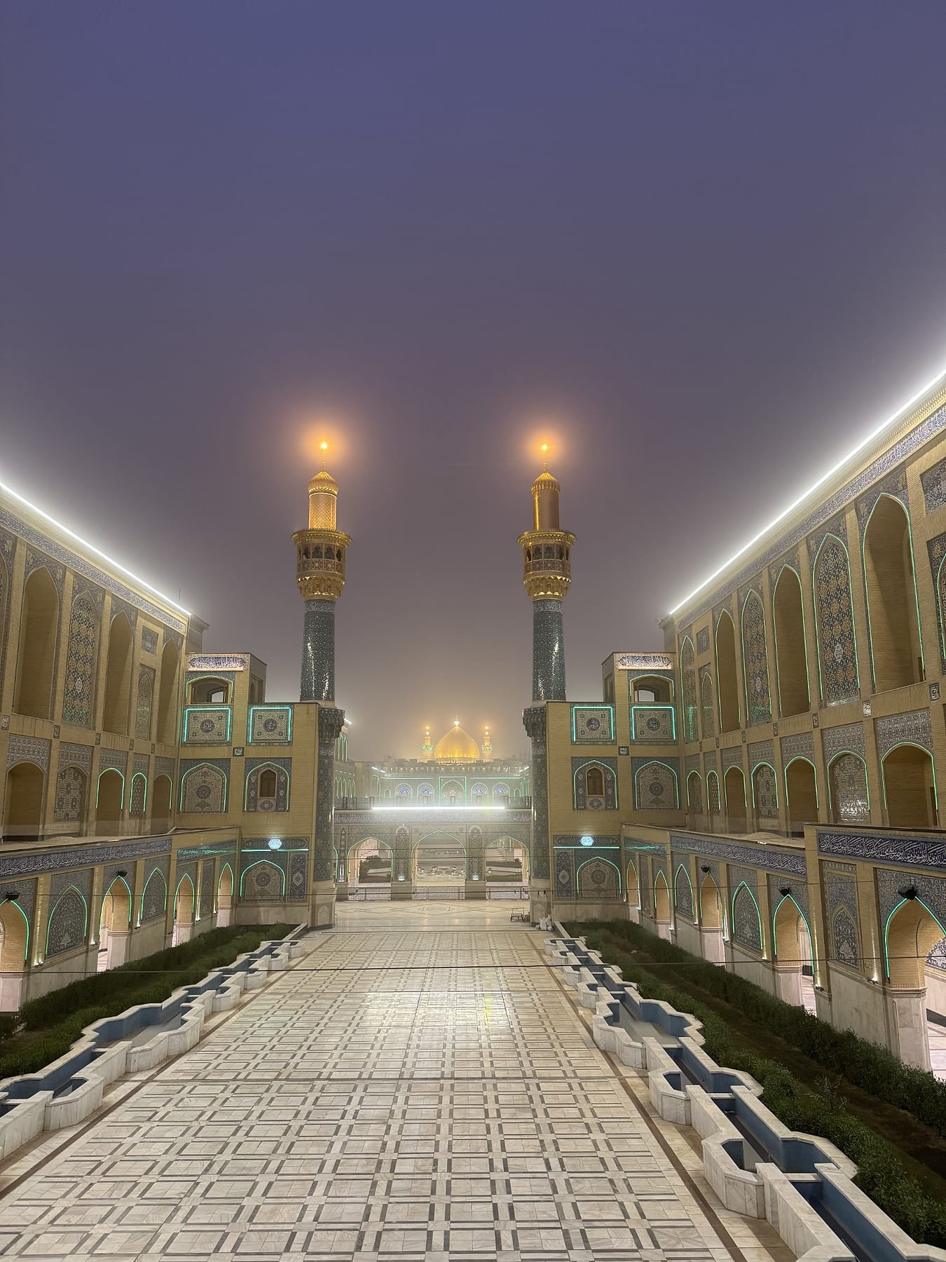 The tiled walkway on a misty night, with the minarets lit at the far end