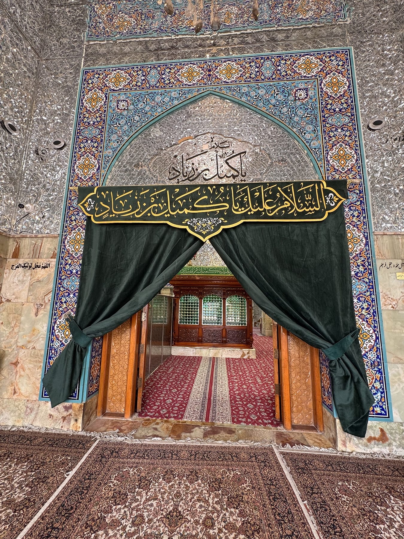A doorway draped with green curtains beneath a tiled arch with Arabic calligraphy